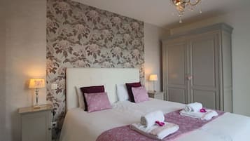 A neatly made bed with a floral-patterned headboard, two bedside lamps, and a wardrobe.