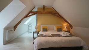 Un dormitorio con techo inclinado, una cama con ropa de cama blanca, dos lámparas de noche y una mesita de noche.