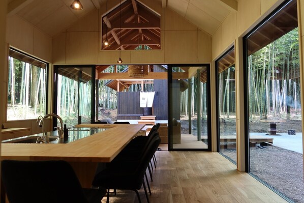 Una cocina moderna con una isla grande, sillas negras y vistas a un bosque a través de amplios ventanales.