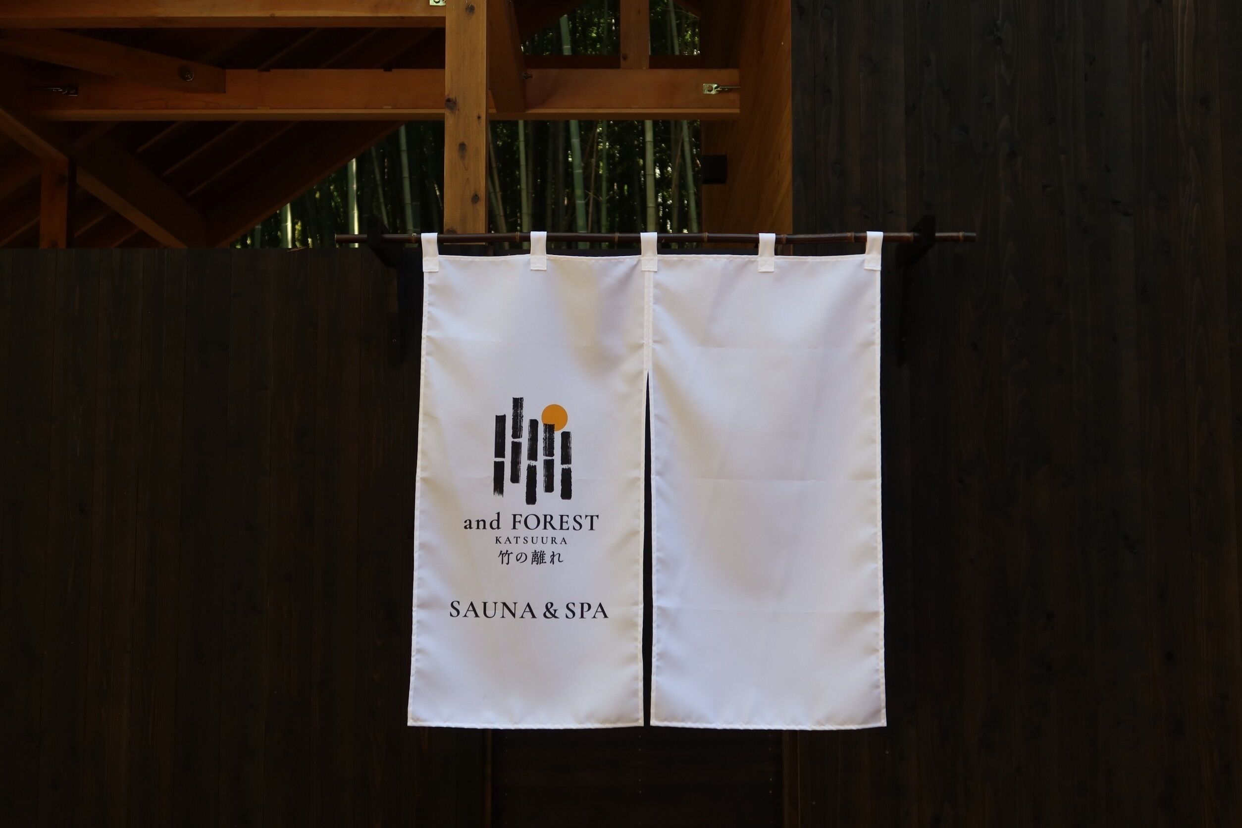 A white banner with the text "and FOREST KATSUURA SAUNA & SPA" hanging on a wooden structure.