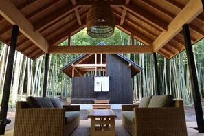 Un área de estar al aire libre cubierta con muebles de mimbre y una mesa central, rodeada por un bosque de bambú.