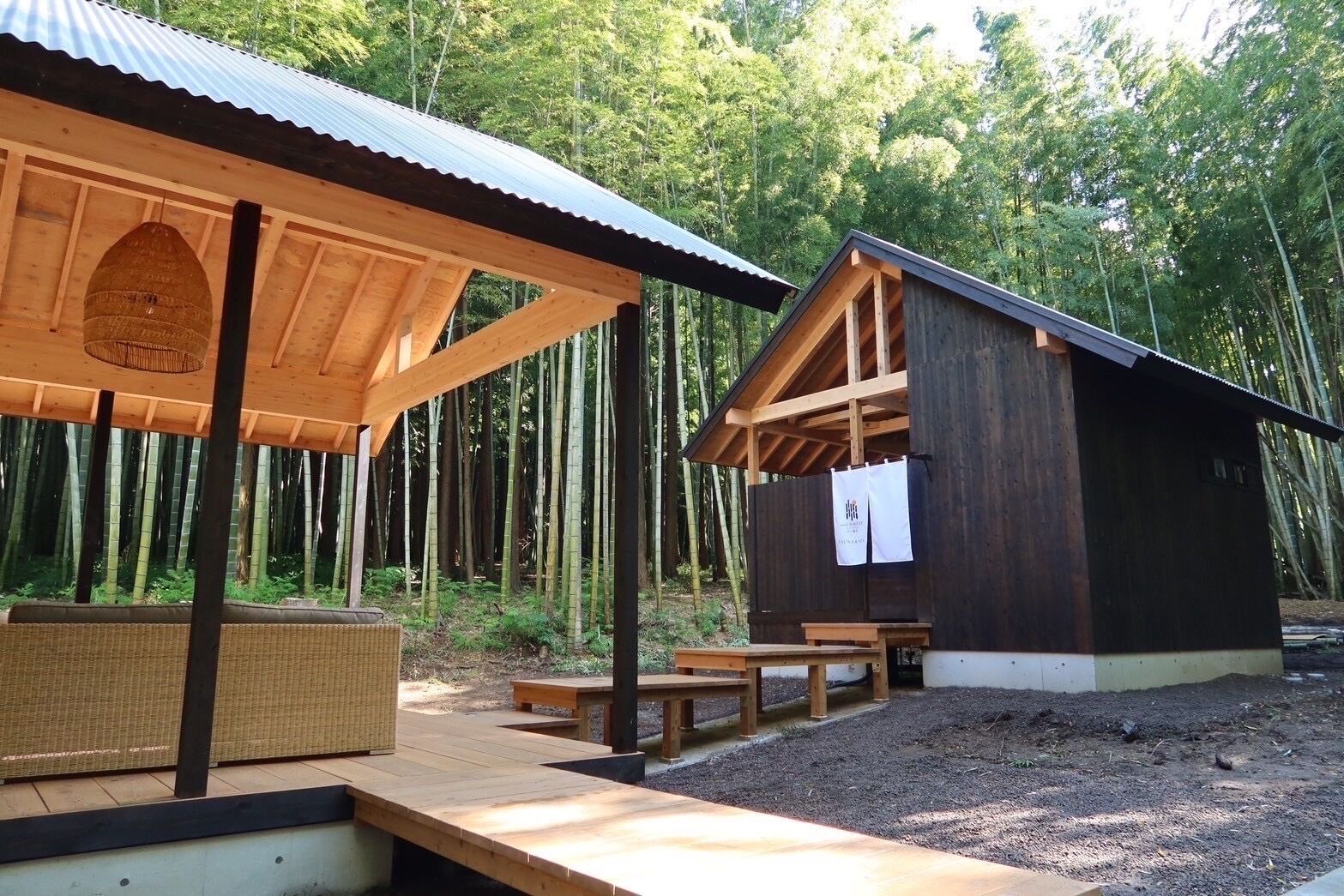 A rustic wooden cabin with a covered porch and picnic tables, surrounded by bamboo forest.