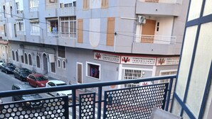 A balcony with a table and chairs, a potted plant, and a view of a street with parked cars and buildings. - Charming 2-bedroom apartment with WiFi, AC in fabulous Torrevieja (Torrevieja)