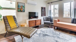 Una sala de estar con un sofá, una silla, un televisor, un aparador y un cuadro.