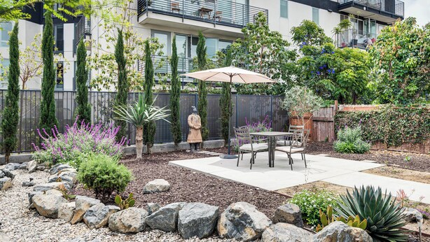 Un patio con mesa y sillas, rodeado de rocas y plantas.