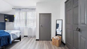 A bedroom with a bed, a wardrobe, a mirror, and a window with blinds.