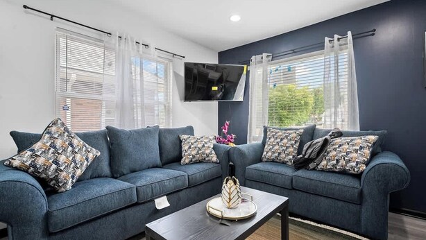A modern living room with a dark blue sofa set, a flat-screen TV mounted on the wall, and a coffee table with decorative items.