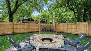 A backyard with a wooden fence, a fire pit, and four lounge chairs.