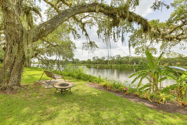 A serene outdoor area with a grassy lawn, a small pond, and a swing chair under a large tree with moss-covered branches. - Boat Lift & Private Dock: Riverfront LaBelle Gem (LaBelle)