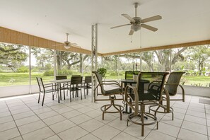 A spacious patio area with a dining table and chairs, ceiling fans, and large windows offering a view of a lush garden. - Boat Lift & Private Dock: Riverfront LaBelle Gem (LaBelle)