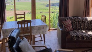 A room with a dining table, chairs, a sofa, and a large window with a countryside view. - The Bothy -  a cottage that sleeps 4 guests  in 2 bedrooms (Lumphanan)