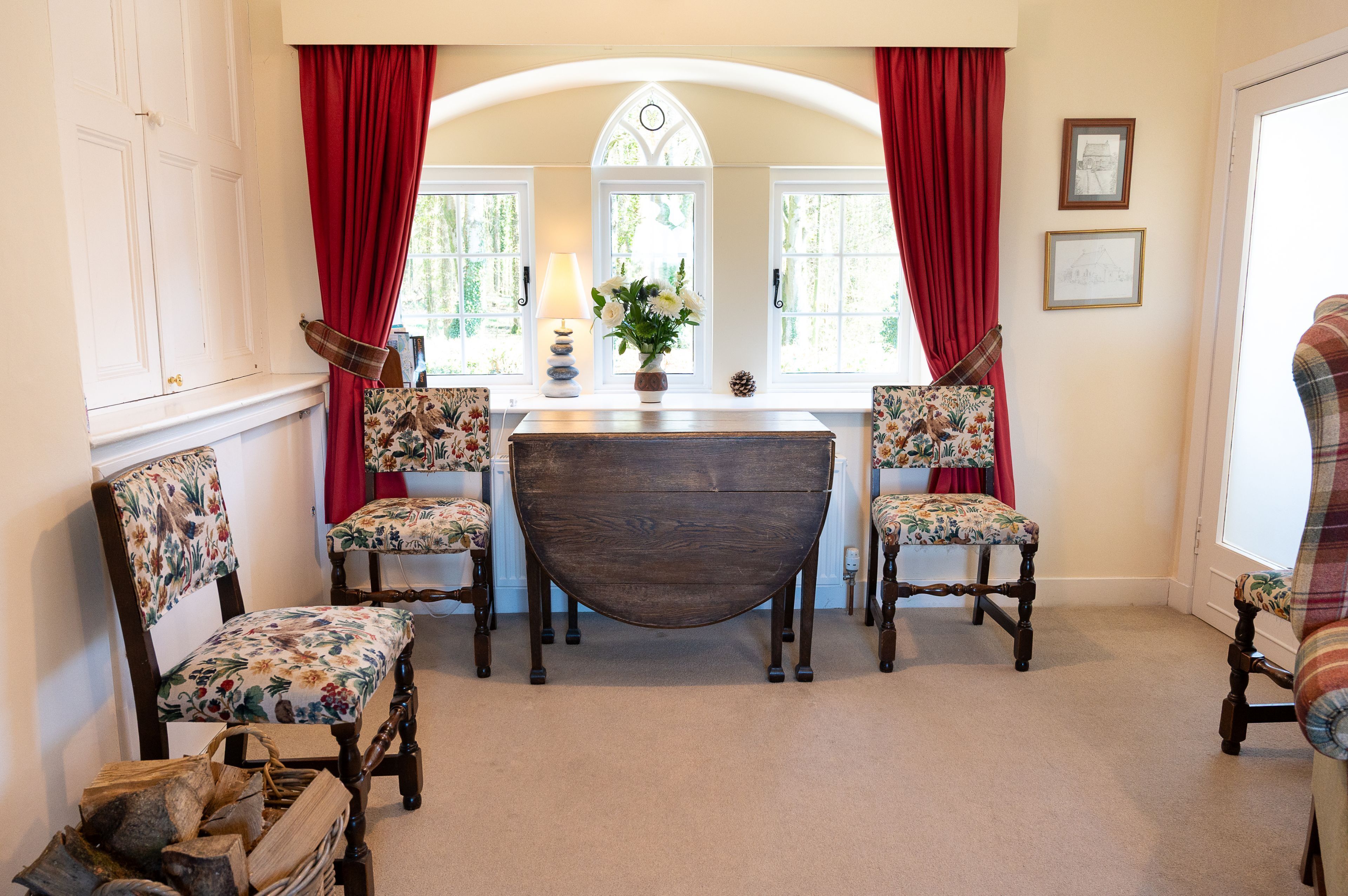 A dining area with a wooden table, floral upholstered chairs, and a red curtain backdrop.