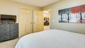 Une chambre à coucher avec un lit, une commode, un téléviseur et un tableau accroché au mur.