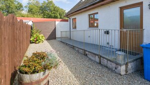 A small house with a gravel driveway, a wooden fence, and a metal railing. - Broombank Cottage - sleeps 6 guests  in 3 bedrooms (Inverness)