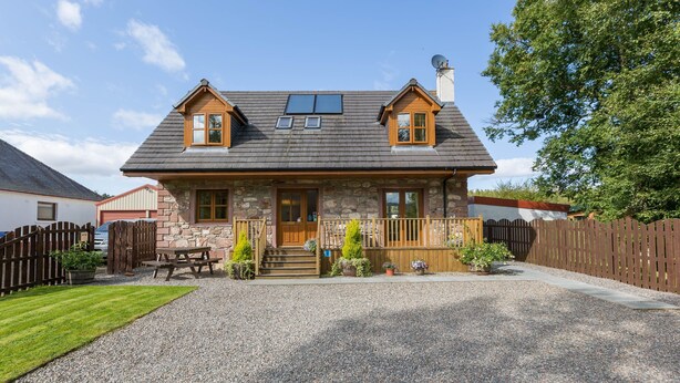A two-story stone house with a gravel driveway, wooden deck, and a fenced backyard. - Broombank Cottage - sleeps 6 guests  in 3 bedrooms (Inverness)