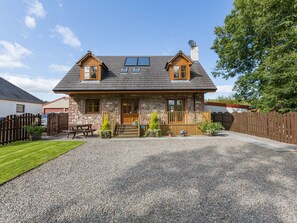 A two-story stone house with a gravel driveway, wooden deck, and a fenced backyard. - Broombank Cottage - sleeps 6 guests  in 3 bedrooms (Inverness)