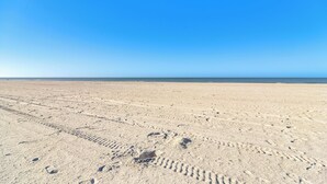 Ein weiter, leerer Sandstrand mit sichtbaren Fußabdrücken und Radspuren.