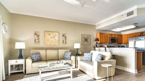 A modern living room with a sofa, coffee table, and a kitchen area with wooden cabinets and appliances. - Treasure Island Condo w/ Bay-View Balcony! (Treasure Island)