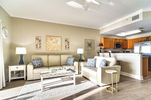 Ein modernes Wohnzimmer mit einer Couch, einem Couchtisch und einer Küchenzeile mit Holzschränken und Geräten.