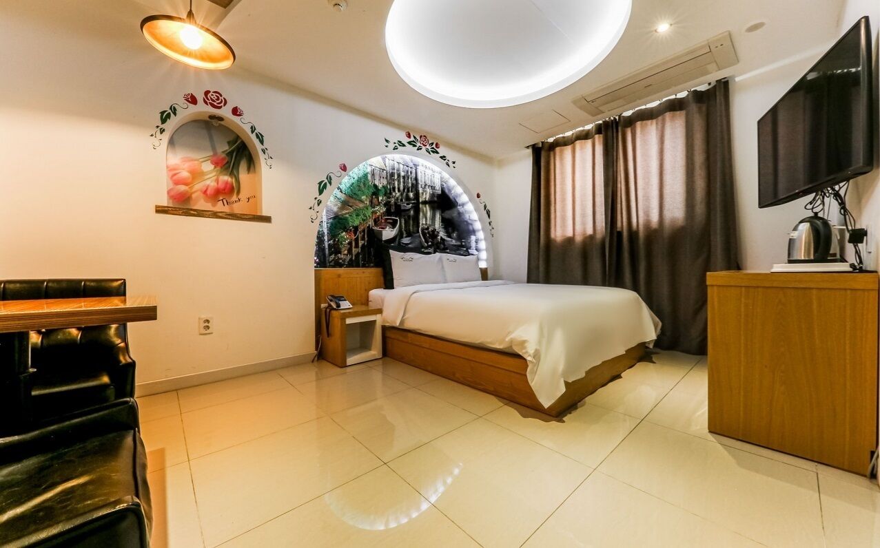A hotel room with a bed, bedside table, TV, and a desk with a chair.