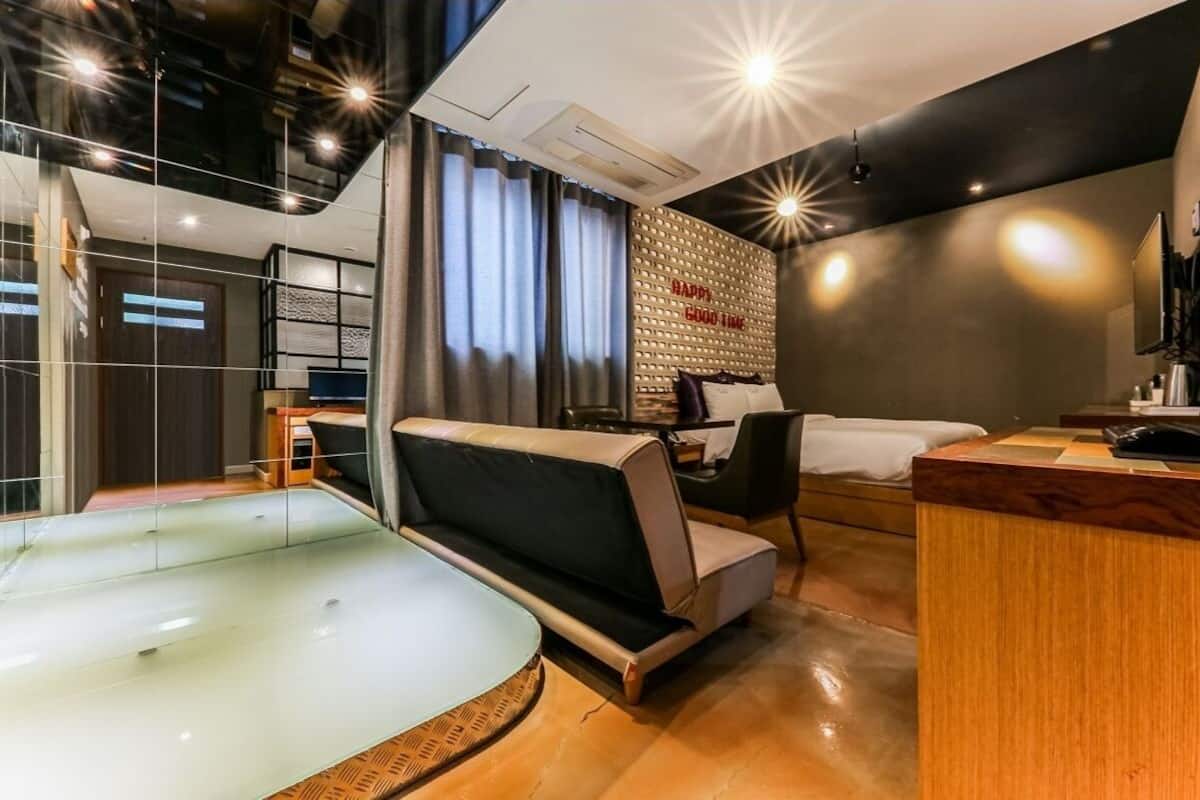 Habitación de hotel moderna con jacuzzi de vidrio, un sofá, un escritorio y un televisor de pared.