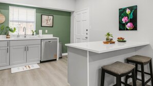 A modern kitchen with a white countertop, grey cabinets, and a green accent wall.