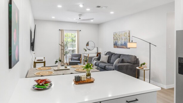 A modern living room with a white island, grey sofa, and a dining area with a table and chairs.