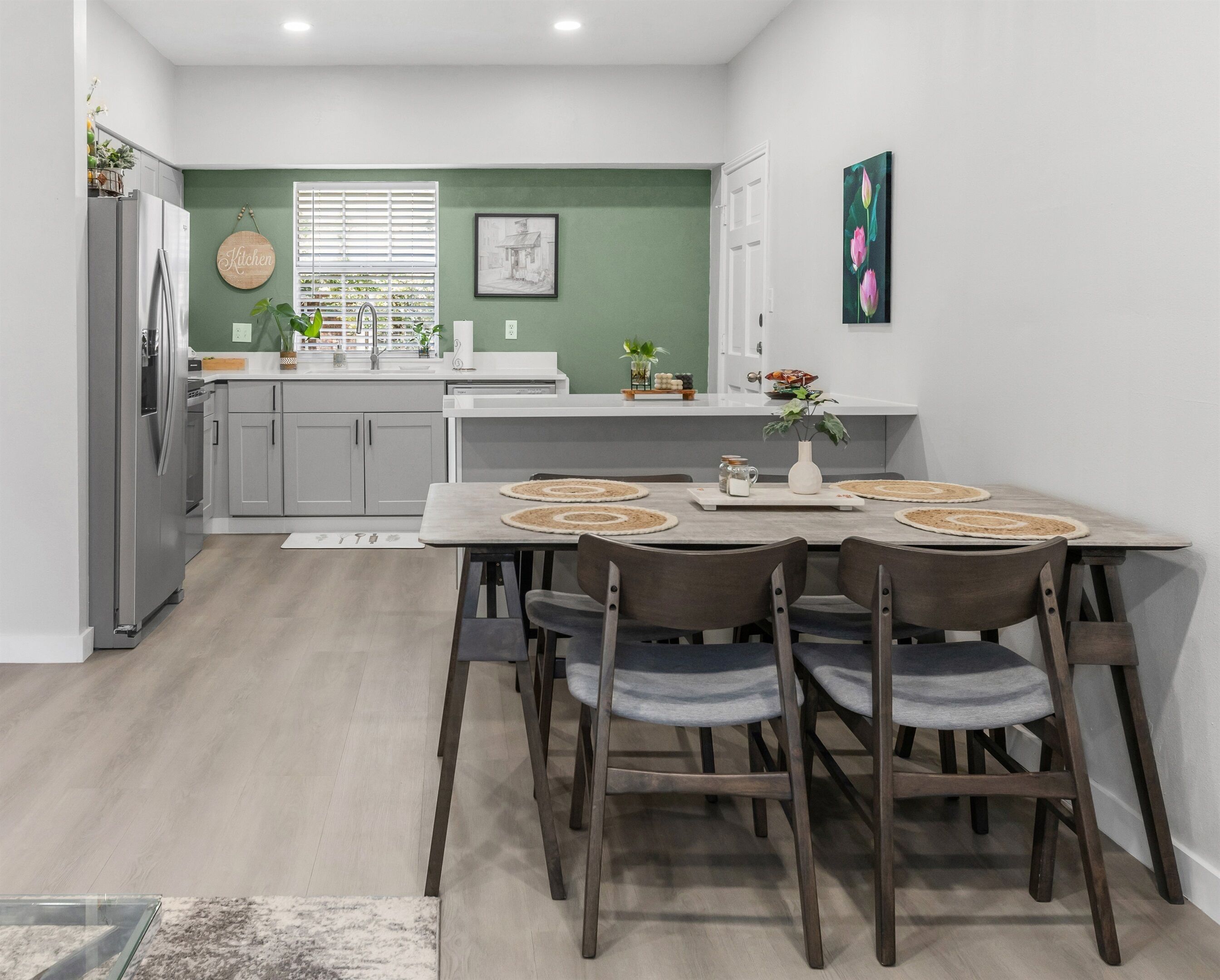 A modern kitchen with a dining area, featuring a refrigerator, cabinets, a sink, and a dining table with chairs.