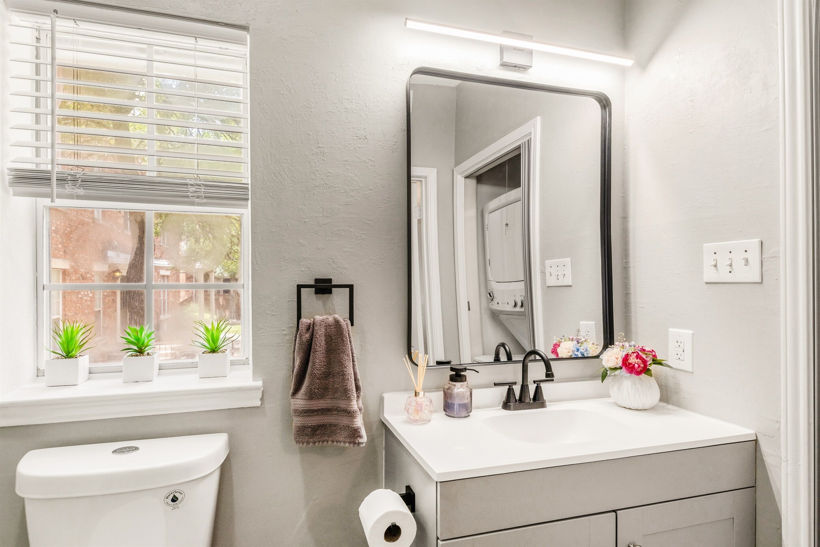 A bathroom with a toilet, sink, mirror, and window with blinds.