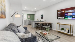 A modern living room with a gray sofa, a glass coffee table, and a dining area with a wooden table and chairs.