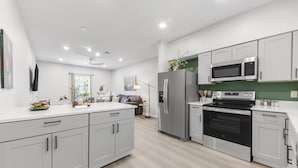 A modern kitchen with white cabinets, stainless steel appliances, and a green backsplash.