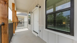 Eine überdachte Veranda mit Betonboden, Holzstützen und einem schwarzen Metallgeländer.