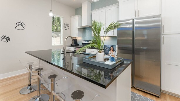 A modern kitchen with white cabinets, a stainless steel refrigerator, and a black granite island with bar stools.