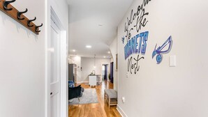 A hallway with a welcome sign, a coat rack, and a view into a living area with a sofa and a rug.