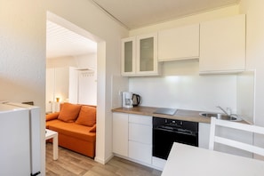 Cocina compacta con armarios blancos, cafetera y lavavajillas.