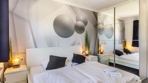 A modern hotel room with a large bed, a nightstand with a lamp, a mirror, and a wall with abstract design. - Holiday Home 'Kugel' with Private Terrace and Wi-Fi (Niedenstein)