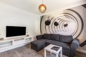 Una sala de estar moderna con un sofá seccional, un televisor de pantalla plana, una mesa de centro blanca y un diseño de pared circular único.