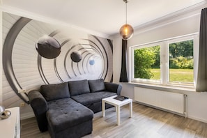 Una sala de estar moderna con un sofá seccional, una mesita blanca y un amplio ventanal con vistas a la vegetación.