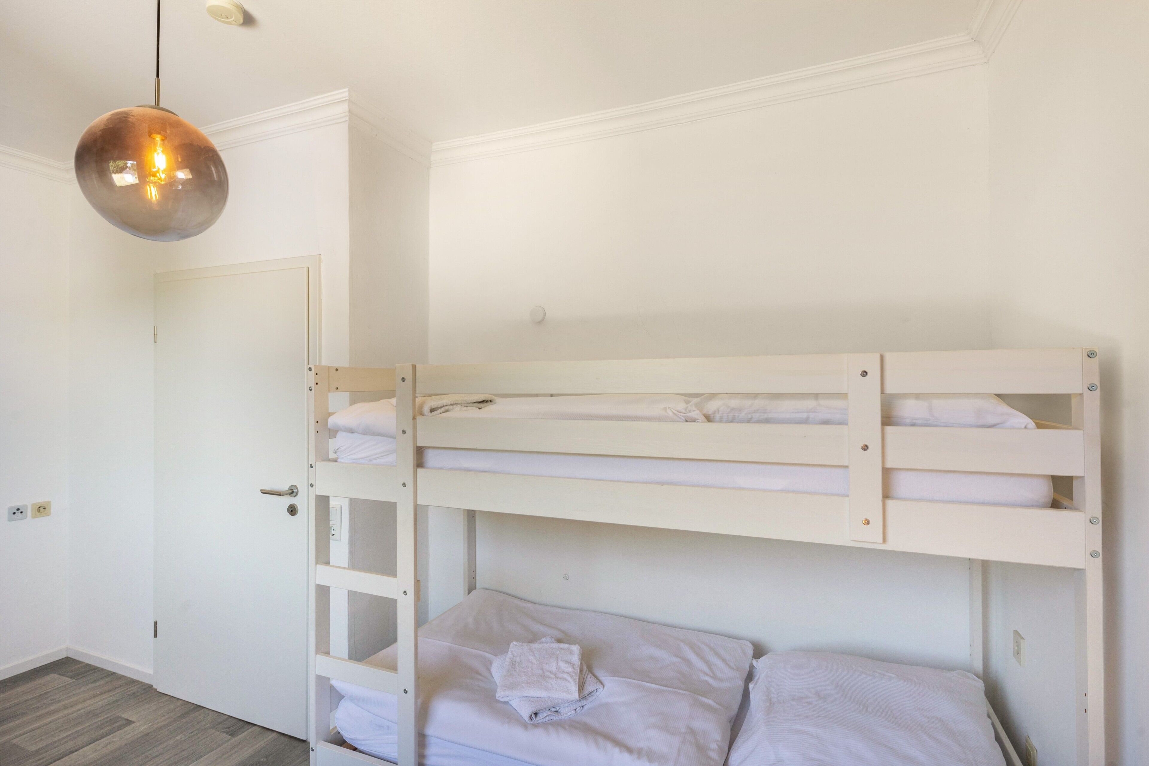A bunk bed room with a door, a light fixture, and a wooden floor.