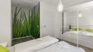 Une chambre moderne avec un grand miroir, un lit avec une literie blanche, une table de chevet avec une lampe et une plante verte.