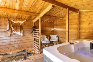Een houten blokhutinterieur met een jacuzzi, bont tapijten en een houten plafond.