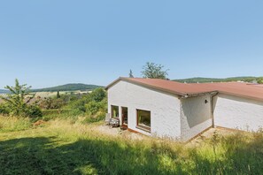 Un bâtiment blanc avec un toit rouge, une terrasse avec une table et des chaises, et une vue sur la campagne.