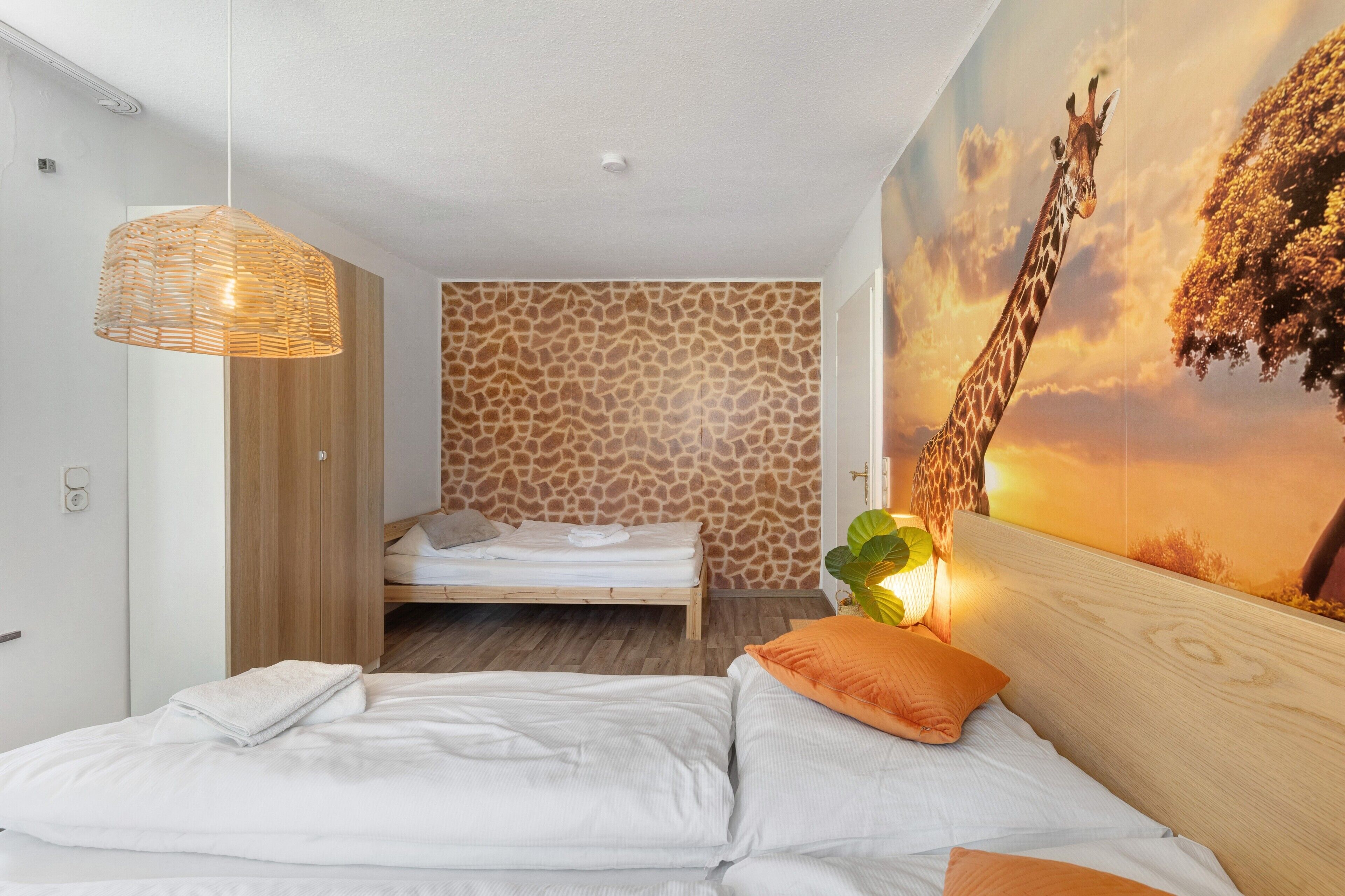 A bedroom with a bed, a hanging light fixture, a giraffe mural, and a wooden wardrobe.