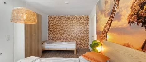 A bedroom with a bed, a hanging light fixture, a giraffe mural, and a wooden wardrobe.
