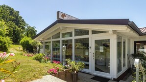 A building with a glass entrance, a sign above the door, and a garden area with flowers and plants. - Holiday Home 'Giraffe' with Private Terrace and Wi-Fi (Niedenstein)