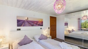 A modern bedroom with two beds, a large mirror, and a lavender field painting.
