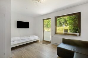 A modern room with a bed, a sofa, a TV, and large windows with a view of greenery. - Bungalow 'Leopard' with Shared Terrace, Shared Garden and Wi-Fi (Niedenstein)