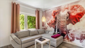 A modern living room with a grey sofa, a white coffee table, a large mural of an elephant, and a hanging light fixture.
