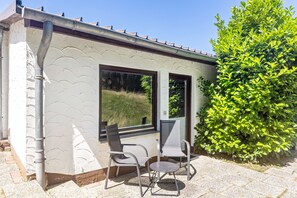 A small building with two windows, a metal chair, a round table, and a green bush. - Holiday Home 'Büffel' with Private Terrace and Wi-Fi (Niedenstein)