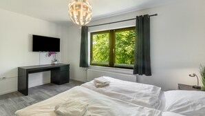 Une chambre à coucher avec un lit, un bureau, une télévision et une fenêtre avec des rideaux.